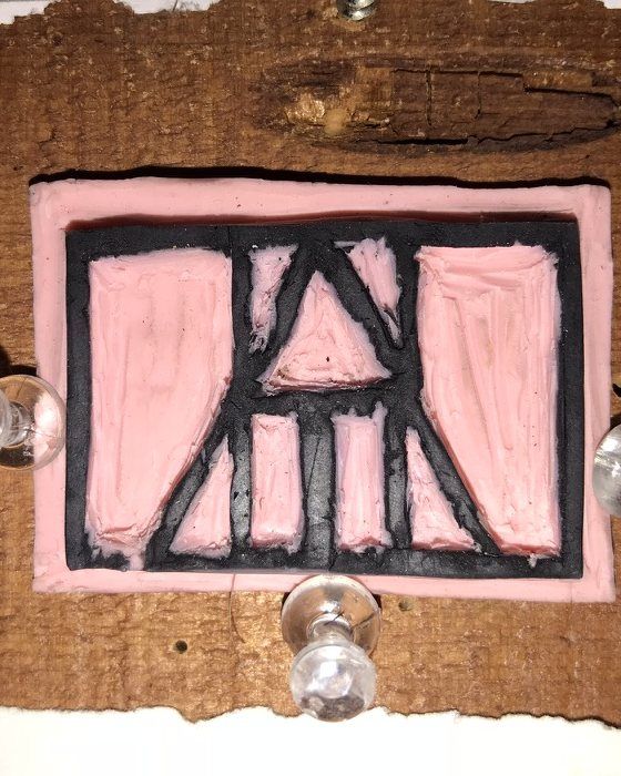 A pink rubber block carved with the HurffHaus mark, pinned to a wooden board.